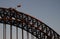 Historic steel truss arch bridge with crane, Australian and New South Wales flags on top. Iconic Sydney Harbor Bridge at dusk.