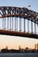 Historic steel truss arch bridge with crane, Australian and New South Wales flags on top. Iconic Sydney Harbor Bridge at dusk.