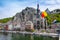 The historic town of Dinant with the Belgian flag and the citadelle on the rock and Collegiate Church of Notre-Dame at the Meuse