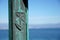 Historical coat of arms with anchor and oars, engraved on an iron pillar in front of the blue sea blurred background