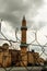 Historical minaret behind fence in Nicosia, capital city of Cyprus. Religious tower with clouds. Column into sky. Historical