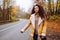 Hitchhiker afro haired woman waiting for a car on the road in the forest at autumn. Woman wearing yellow jacket