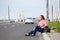 Hitchhiking, passenger car driving along, woman sitting roadside with backpack