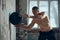 Hitting ball on wall. Young muscular man with strong, relief body shape training shirtless with fitness ball indoors