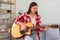 Hobby concept, Young asian woman learning and practice playing chords with acoustic guitar on couch