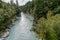 Hokitika River flowing to coast through steep Hokitika Gorge between rock sides and native forest and red rata flower