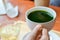 Hold hot matcha green tea in white ceramic cup on hand served on wooden tray on table in cafe and coffee shop. Healty beverages