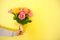 holding beautiful tender blossoming bouquet of yellow and pink roses on yellow background. Man delivers flowers at home