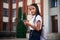 Holding smartphone. School girl in uniform is outdoors near the building