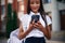 Holding smartphone. School girl in uniform is outdoors near the building