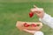 Holding strawberry in hand. Strawberries in disposable eco plate on green background. Seasonal red berry