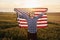 Holding USA flag in hands. Patriotic senior stylish man with grey hair and beard on the agricultural field