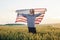 Holding USA flag in hands. Patriotic senior stylish man with grey hair and beard on the agricultural field