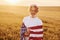 Holding USA flag in hands. Patriotic senior stylish man with grey hair and beard on the agricultural field