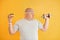 Holds hamburger and dumbbell. Funny overweight man in sportive head tie is against yellow background