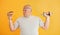 Holds hamburger and dumbbell. Funny overweight man in sportive head tie is against yellow background