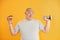 Holds hamburger and dumbbell. Funny overweight man in sportive head tie is against yellow background