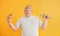 Holds hamburger and dumbbell. Funny overweight man in sportive head tie is against yellow background