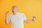 Holds hamburger and dumbbell. Funny overweight man in sportive head tie is against yellow background