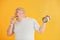 Holds hamburger and dumbbell. Funny overweight man in sportive head tie is against yellow background