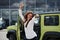 Holds keys of her new vehicle. Young woman in white official clothes dancing in front of green automobile outdoors