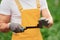 Holds plant on little showel. Young greenhouse worker in yellow uniform have job inside of hothouse