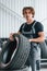 Holds tire. Adult man in grey colored uniform works in the automobile salon