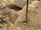 A hole dug in the ground with a shovel nearby. Place in the sand at the cemetery. Burial grave dug with a shovel