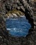 Hole in icelandic black lava rock formation with atlantic ocean in background