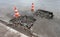 Holes and damage on an asphalt road, secured by red and white shut-off cones because of the risk of accidents