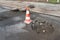 Holes and damage on an asphalt road, secured by red and white shut-off cones because of the risk of accidents