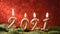 Holiday background Happy New Year 2021. Digits of year 2021 made by burning gold candles on red festive sparkling background.