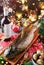 Holiday baked whole fish on wooden board on red napkin served with glasses, bottle of wine, candles, fir branches, festive