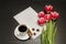 Holiday concept. Bouquet of pink tulips, a cup of coffee, cinnamon, star anise and sheet of paper on a black wooden background