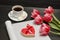 Holiday concept. Bouquet of pink tulips, a cup of coffee, red heart-shaped cookies with a note, empty magazine on a black wooden