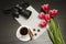 Holiday concept. Bouquet of pink tulips, dslr camera, cup of coffee, cinnamon, star anise and sheet of paper on a black wooden