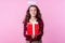 Holiday discounts. Portrait of charming angelic teenage girl with toy halo above her head holding out gift box. pink background