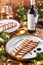 Holiday dish of sliced baked meat with sauce in plate on wooden table served with plate, glasses, bottle of wine, candles, fir