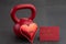 Holiday fitness, red kettlebell, with a metal red heart, on a black gym floor, with red valentine card