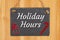 Holiday Hours type message on hanging chalkboard sign with a candy cane and gift