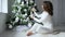 Holiday morning, girl with brown hair decorates festive Christmas tree in soft white tones