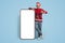 Holiday Offer. Joyful Guy In Santa Hat Standing Near Big Blank Smartphone