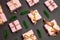 Holiday pattern of assorted gifts wrapped in a pink thought with a gold awning and green sprigs of fir on a dark background. Top