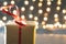 Holiday present with brown wrapping paper and a bright red ribbon with a bokeh Christmas light background and copy space