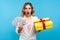Holiday sales. Portrait of amazed joyous woman holding bunch of dollars and wrapped present box. blue background