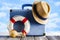 Holiday suitcase, summer hat, lifebuoy and shells on beach background