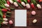 Holiday template. Tulip flowers, empty blank of paper, pen, french macaroons pastries and cup of coffee on a dark wooden