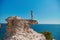 Holiday time. Summer adventure. Beach vacation. Woman standing on sharp cliff. Breathtaking seascape. Cloudless sky