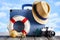 Holiday travel concept - suitcase, summer hat, photo camera, lifebuoy and shells on beach and wooden background