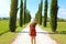 Holiday in Tuscany. Young happy woman in red dress and hat walking on pathway with typical Tuscany landscape. Girl enjoying view